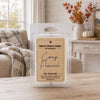 A packaged soy wax melt labeled 'Cozy Flannel' by Country Crackle Candle, shown in a clear plastic clamshell package on a wooden table in a softly styled living room setting.