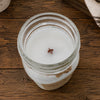 A top-down view of a white soy wax candle in a clear glass jar with a small wooden wick, set on a rustic dark wood surface.