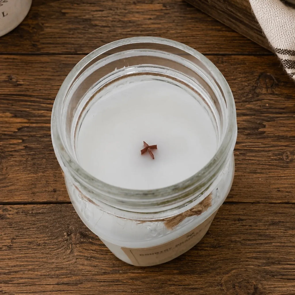 A top-down view of a white soy wax candle in a clear glass jar with a small wooden wick, set on a rustic dark wood surface.